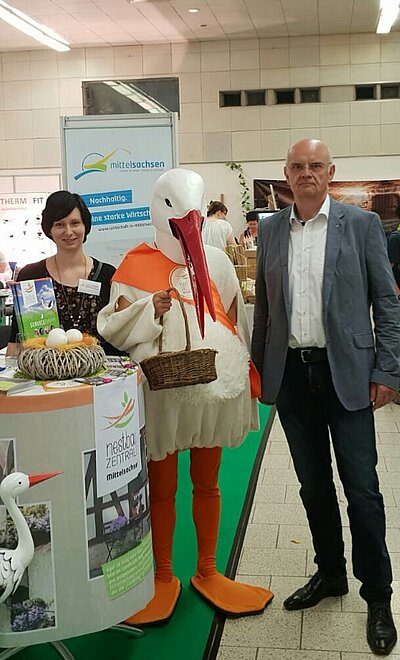 Dr. Lothar Beier mit Nestbaukoordinatorin Josefine Tzschoppe und dem Storch am Mittelsachsenstand zur Messe Land und Genuss in Leipzig.